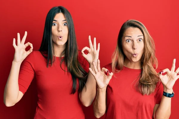 西班牙裔家庭的母亲和女儿穿着红色背景的休闲装 看上去很惊讶 很震惊 用手指做了个认可的标志 疯狂的表达 — 图库照片