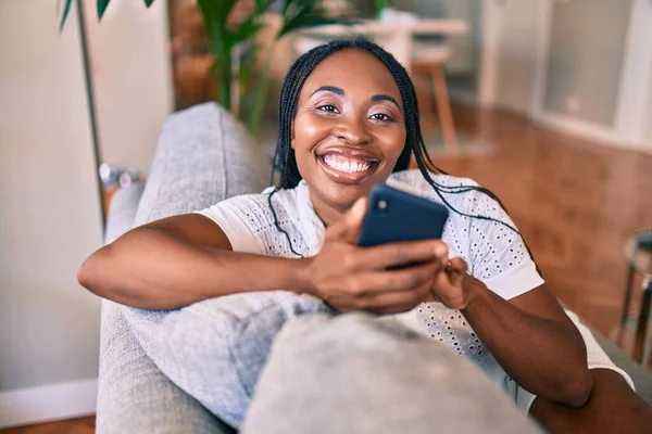 Joven Mujer Afroamericana Sonriendo Feliz Sentado Usando Teléfono Inteligente Casa —  Fotos de Stock