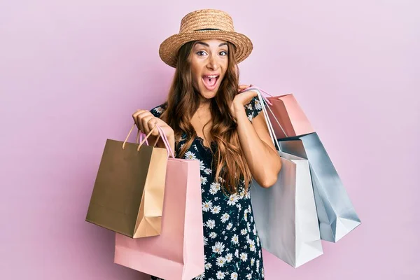 Young brunette woman holding shopping bags celebrating crazy and amazed for success with open eyes screaming excited.