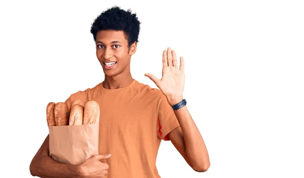 Young African American Man Holding Paper Bag Bread Waiving Saying — Stock Photo, Image