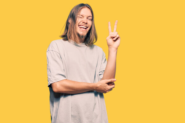 Handsome caucasian man with long hair wearing casual clothes smiling with happy face winking at the camera doing victory sign. number two. 