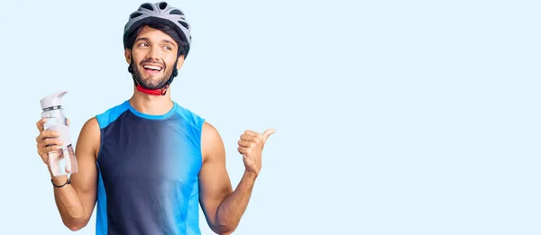ハンサムなヒスパニック系の男身に着けています自転車ヘルメットと保持水ボトル指差す親指へ側笑顔幸せなでオープン口 — ストック写真