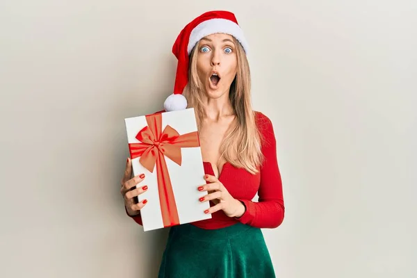 Krásná Běloška Nosí Vánoční Klobouk Drží Dárek Vyděšený Ohromený Otevřenými — Stock fotografie