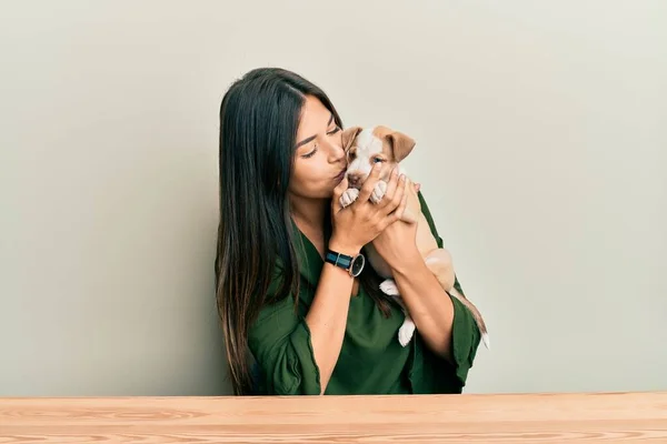 Menina Hispânica Jovem Abraçando Beijando Cão Sentado Mesa Sobre Fundo — Fotografia de Stock