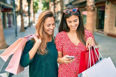 Güzel İspanyol anne ve kızı akıllı telefon kullanıyor ve şehirde alışveriş yapıyor..