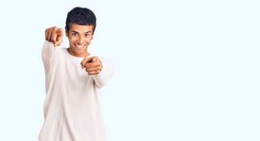 Genç Afro-Amerikan adam günlük giysiler içinde seni ve kamerayı parmaklarıyla göstererek mutlu ve mutlu bir şekilde gülümsüyor. 