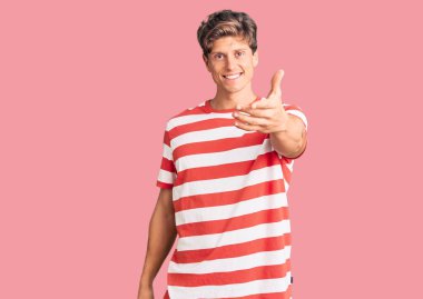 Gündelik kıyafetler giyen genç yakışıklı adam dostça bir selamlama ve hoş geldin hediyesi olarak el sıkışmayı sunuyor. başarılı iş. 