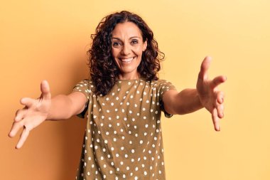 Orta yaşlı, güzel bir kadın, sıradan bir tişört giyip kameraya bakıyor. Sarılmak için kollarını açmış gülümsüyor. Mutluluğu kucaklayan neşeli bir ifade.. 