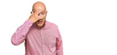 Orta yaşlı, kel bir adam. Şoka girmiş, yüzünü ve gözlerini kapamış, utanmış bir ifadeyle parmaklarının arasından bakıyor.. 