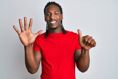 Saçları örgülü Afro-Amerikalı bir adam, altı numaralı parmaklarını gösterip gösterirken kendinden emin ve mutlu gülümsüyor.. 