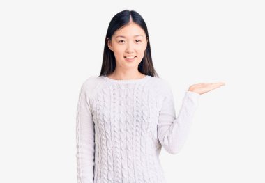 Gündelik süveter giyen, neşeli gülümseyen, avuç içi kameraya bakan genç ve güzel bir Çinli kadın.. 