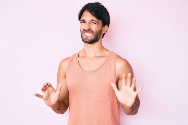 Yakışıklı İspanyol bir adam günlük giysiler giyiyor, tiksindirici bir ifade takınıyor, tiksindirici bir yüz ifadesi takınıyor ve tiksindirici bir ifade takınıyor. Eller havada. 