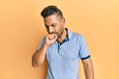 Sakallı, sıradan kıyafetler giyen, kendini kötü hisseden ve soğuk algınlığı veya bronşitin belirtisi olarak öksüren yakışıklı bir adam. sağlık hizmeti kavramı. 