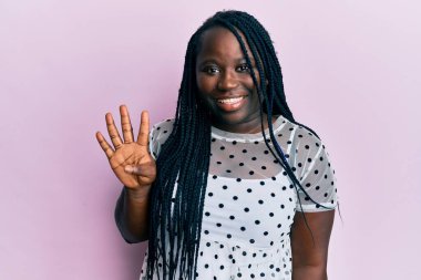 Saçları örgülü genç siyahi kadın dört numarayı gösterip gösterirken kendinden emin ve mutlu bir şekilde gülümsüyor.. 