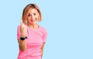 Spor kıyafeti giyen genç sarışın kadın seni buraya çağırıyor. El kol hareketi yap. Mutlu bir şekilde karşıla ve gülümse. 