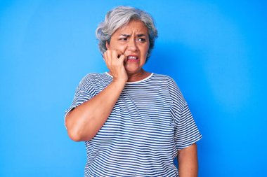 Son sınıf İspanyol asıllı, gri saçlı, günlük kıyafetler giyen, gergin ve elleri ağızdan tırnak yiyen bir kadın. anksiyete. 