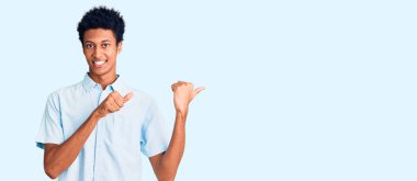 Gündelik giysiler giymiş genç Afro-Amerikan bir adam arka tarafı işaret ediyor. Elleri havada, kendinden emin gülümsüyor. 