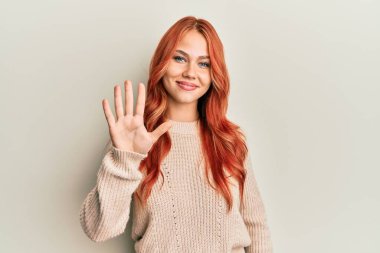 Genç, güzel, kızıl saçlı, sıradan bir süveter giyen, beş numaralı parmaklarıyla işaret eden, kendinden emin ve mutlu bir şekilde gülümseyen kadın.. 