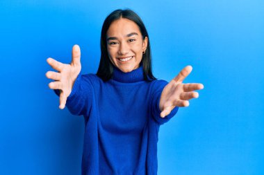 Sıradan bir kazak giyen Asyalı genç bir kadın kameraya sarılıp gülümseyerek bakıyor. Mutluluğu kucaklayan neşeli bir ifade.. 