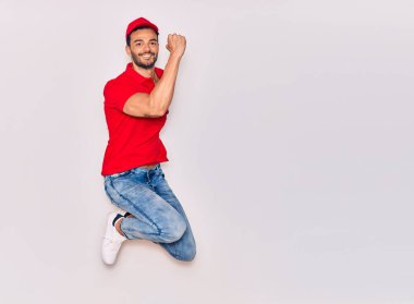 Mutlu gülümseyen üniformalı yakışıklı İspanyol teslimatçı. Yüzünde tebessümle zıplıyor, beyaz arka planda yumruklar havada kutluyor..