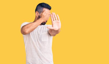 Latin kökenli genç bir adam, günlük kıyafetler giyip, elleriyle gözlerini kapatıyor ve üzgün ve korku ifadeleriyle jestleri durduruyor. utangaç ve olumsuz kavram. 