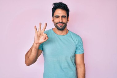 Yakışıklı, sakallı, sıradan kıyafetler giyen, üç numaralı parmaklarıyla işaret eden, kendinden emin ve mutlu bir adam.. 