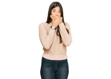 Kış süveteri giyen genç esmer kadın yanlışlıkla elleriyle ağzını kapatırken şok oldu. gizli kavram. 