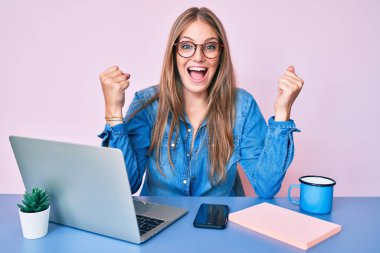 Ofiste çalışan genç sarışın kız bir fincan kahve içiyor gururla bağırıyor, zaferi kutluyor ve kollarını kaldırıp başarıyı kutluyor. 