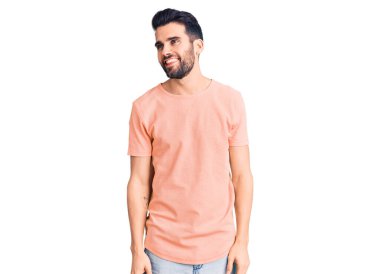 Sakallı, sıradan tişörtlü, yüzünde gülümseme ve doğal ifadeyle yan yana bakan yakışıklı bir genç. Kendinden emin gülen. 