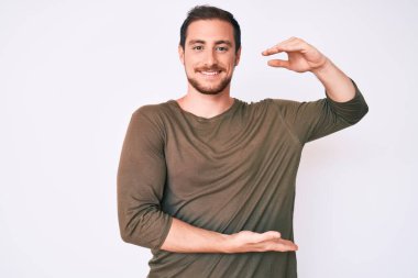 Elleriyle el kol hareketi yapan, büyük ve büyük beden işareti gösteren sıradan kıyafetler giyen genç yakışıklı bir adam. Kameraya bakıp gülümsüyor. ölçüm kavramı. 