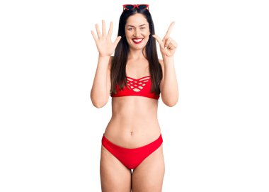 Bikini giyen genç, beyaz bir kadın 7 numaralı parmaklarını gösterip onu gösterirken mutlu ve kendinden emin gülümsüyor.. 