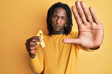 African american man with braids holding suicide prevention yellow ribbon with open hand doing stop sign with serious and confident expression, defense gesture  clipart