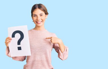 Sarışın, beyaz bir kadın elinde soru işareti tutarak gülümseyen mutlu ve gururlu birini işaret ediyor. 