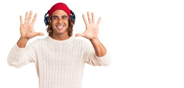 Genç İspanyol adam müzik dinliyor. Kulaklık takıyor ve 10 numaralı parmaklarıyla işaret ediyor. Kendinden emin ve mutlu bir şekilde gülümsüyor.. 