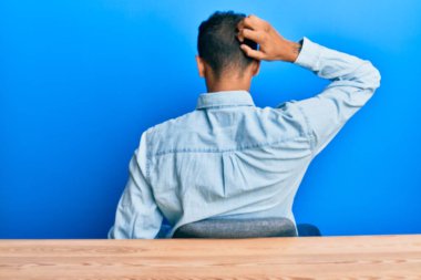 Genç, yakışıklı, Afro-Amerikalı, gündelik giysiler giymiş, masanın arkasında oturmuş, elleri kafasında şüpheyi düşünüyor. 