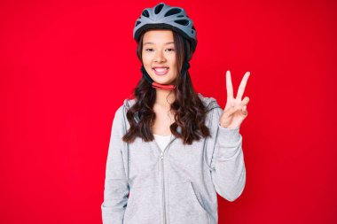 Bisiklet kaskı takan, gülümseyen, kameraya göz kırpan, zafer işareti yapan genç, güzel Çinli bir kız. İki numara.. 