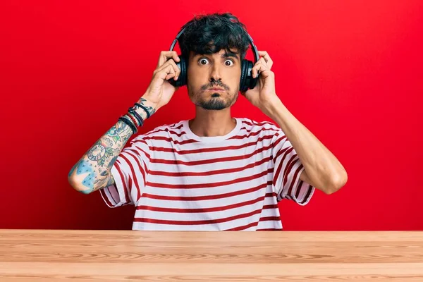 Junger Hispanischer Mann Mit Kopfhörern Der Auf Dem Tisch Sitzt — Stockfoto