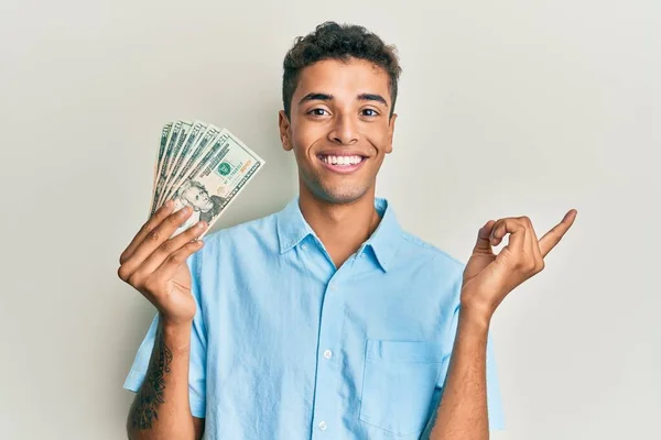 Joven Hombre Afroamericano Guapo Sosteniendo Billetes Dólares Sonriendo Feliz Señalando —  Fotos de Stock