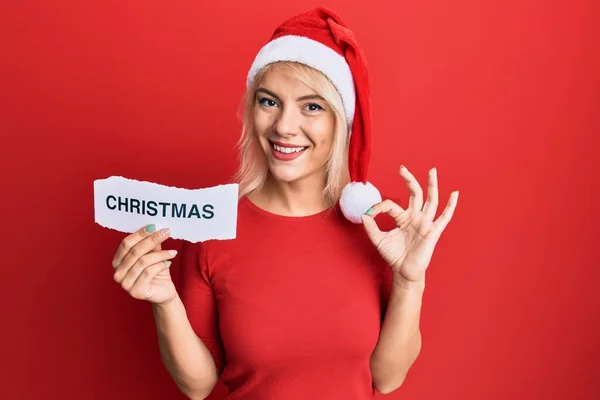 Jovem Loira Vestindo Chapéu Xmas Segurando Papel Com Palavra Natal — Fotografia de Stock