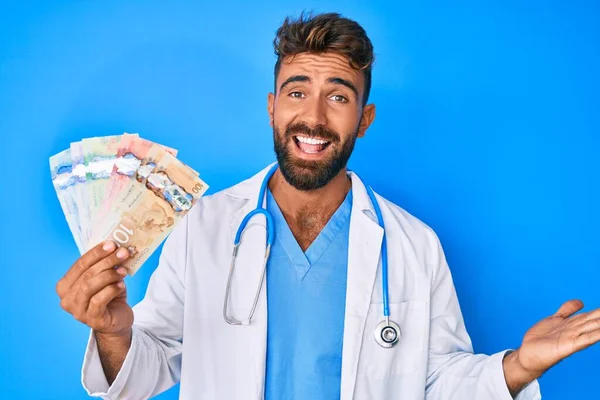 Joven Hombre Hispano Vistiendo Uniforme Médico Sosteniendo Dólares Canadienses Celebrando — Foto de Stock