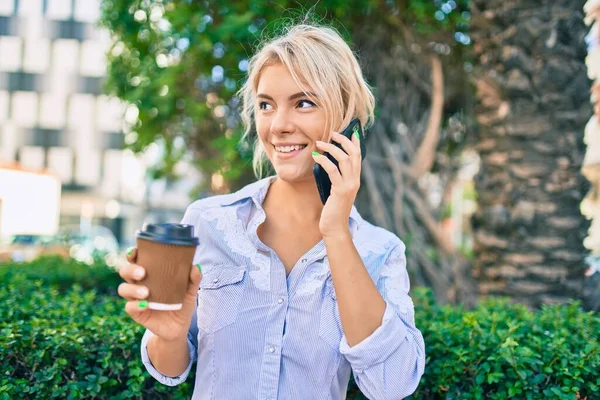 在城市里 年轻的金发女人高兴地一边用智能手机聊天 一边喝着咖啡 — 图库照片