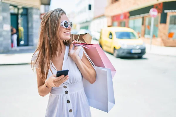 Junge Blonde Frau Lächelt Glücklich Mit Einkaufstüten Und Smartphone Auf — Stockfoto