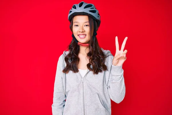 若い美しい中国の女の子は カメラで勝利のサインを行うと 幸せな顔をウィンクと笑みを浮かべて自転車のヘルメットを着ている — ストック写真