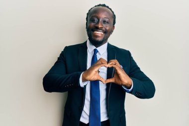 Yakışıklı, takım elbiseli ve kravatlı genç bir adam. Sevgiyle gülümsüyor. Elleriyle kalp sembolü ve şekli gösteriyor. romantik kavram. 