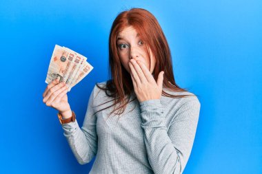 Genç kızıl saçlı kız elinde 10 pound banknot tutuyor. Ağzını eliyle kapatıyor. Şok geçiriyor ve hata yapmaktan korkuyor. şaşırmış ifade 
