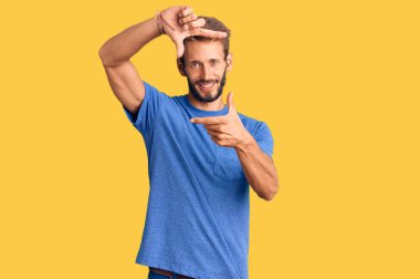 Sarışın, sakallı, sıradan kıyafetler giyen, gülümseyen, elleri ve parmakları mutlu yüzlü yakışıklı bir adam. yaratıcılık ve fotoğrafçılık kavramı. 