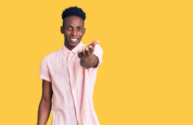 Genç Afro-Amerikan adam günlük kıyafetler giyip gülümseyerek dostça el sıkışarak selamlama ve hoş geldin diyor. başarılı iş. 