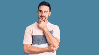 Elleri çenesinde gündelik giysiler giymiş soru soran, düşünceli bir genç adam. Düşünceli bir yüzle gülümsüyor. şüphe kavramı. 