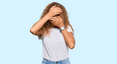 Güzel, beyaz tişört giyen, gözleri ve ağzı elleri kapalı, şaşırmış ve şok olmuş beyaz bir genç kız. duygu gizleme 