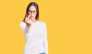 Beautiful brunette young woman wearing casual white sweater and glasses showing middle finger, impolite and rude fuck off expression 